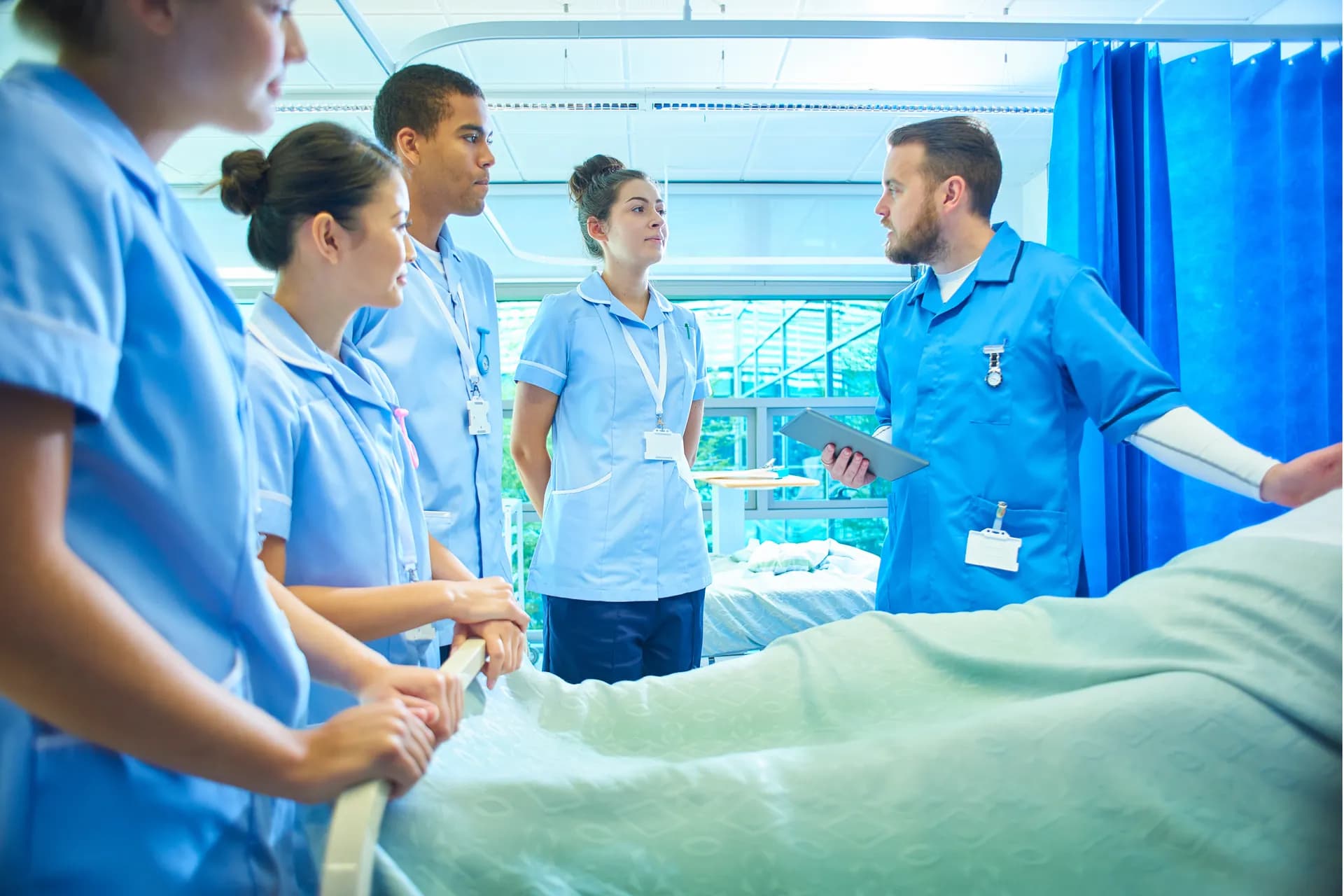 Pflegelehrer leitet praktische Übung mit Auszubildenden am Krankenbett